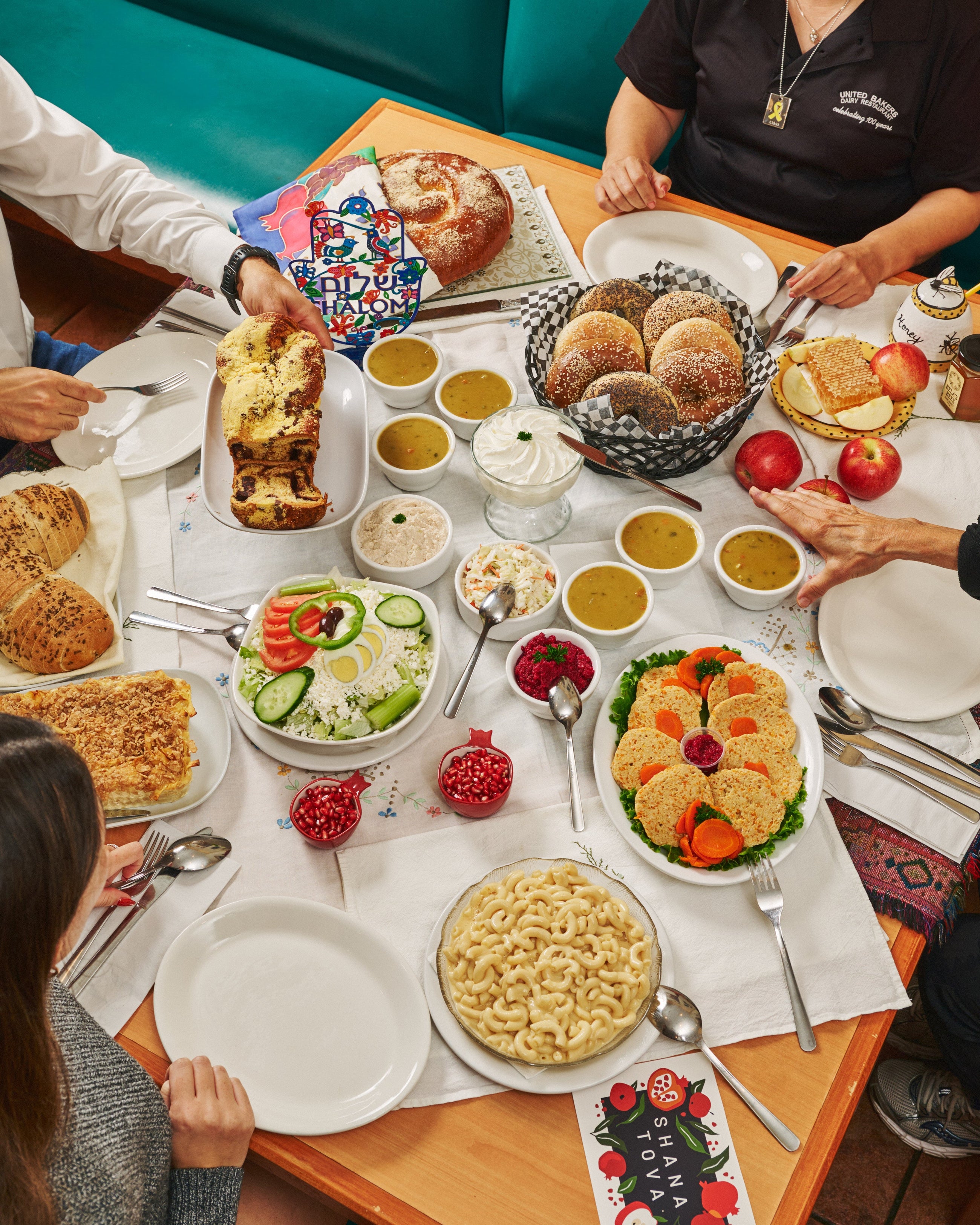 A round challah bread with raisins, partially covered with a white cloth, displayed on a table with apples and honey in the background, suggesting a setting for Rosh Hashanah celebrations.