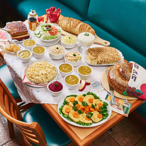 Diner table with various food items including sandwiches, salads, and side dishes on a checkered tablecloth. For Rosh Hashanah Toronto with Gefilte Fish